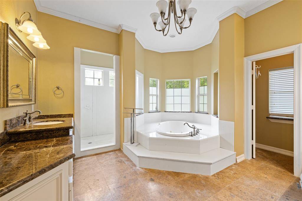 This spacious bathroom features a large soaking tub, a separate walk in shower, dual sinks with granite countertops, and ample natural light from multiple windows. The warm wall color and elegant lighting add a touch of luxury.