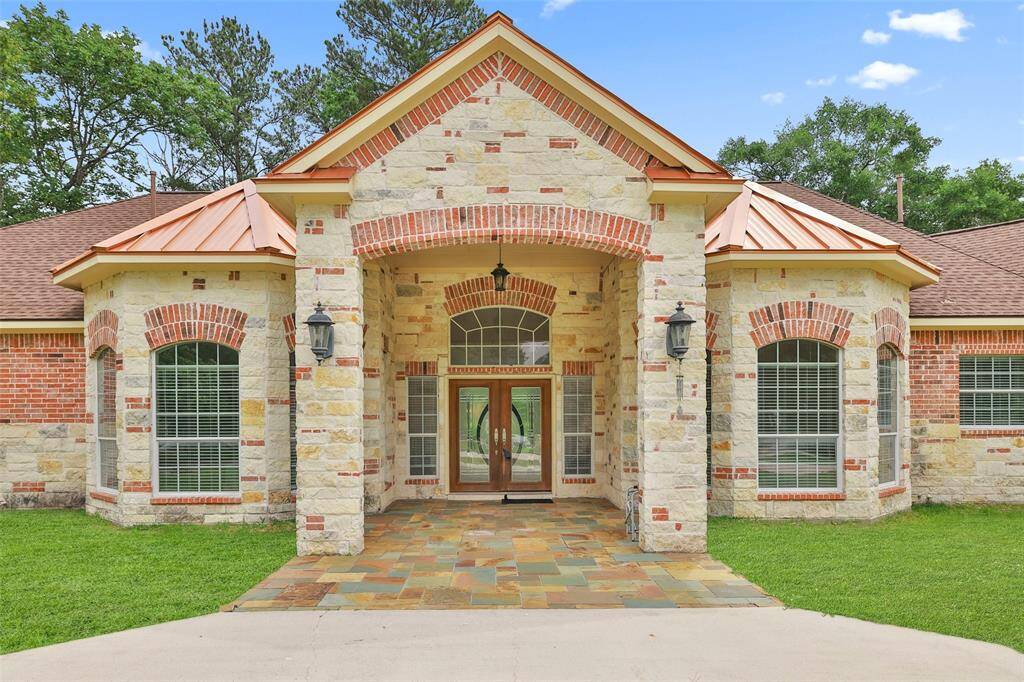This photo showcases a spacious, single-story brick home with a distinctive entrance, double doors, large windows, set against a backdrop of mature trees..
