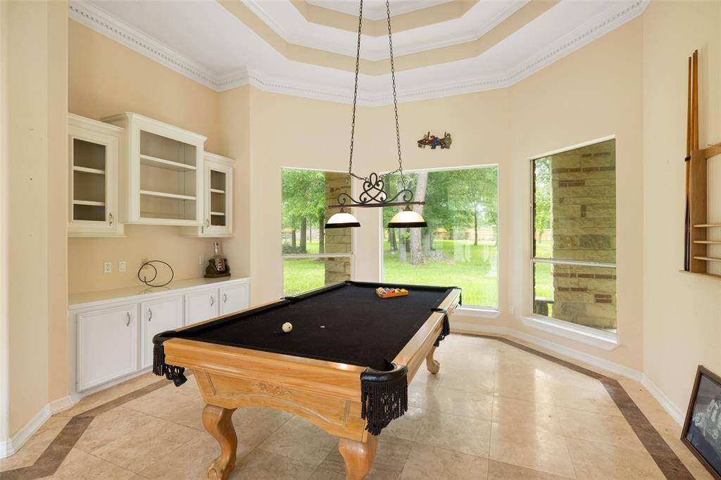 This photo showcases a bright, living room or use as a game room, featuring a tray ceiling and large windows offering scenic views. The space includes built-in cabinets and a stylish light fixture, perfect for entertainment.