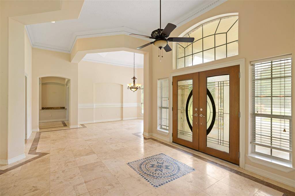 Spacious, elegant entryway with high ceilings and abundant natural light. Features decorative tile flooring, a stylish ceiling fan, and distinctive glass double doors flanked by large windows. Ideal for a welcoming home atmosphere.
