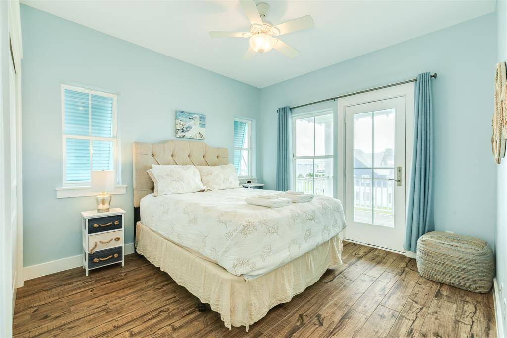Bright and airy bedroom 5 with light blue walls, featuring a cozy bed, and double doors leading to one of 3 decks. It offers a serene and inviting atmosphere.