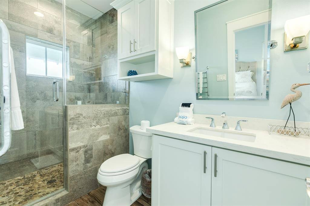 This bathroom features a modern design with a glass-enclosed shower, tile accents, and a sleek vanity with ample storage. Natural light enhances the clean, airy feel of the space.