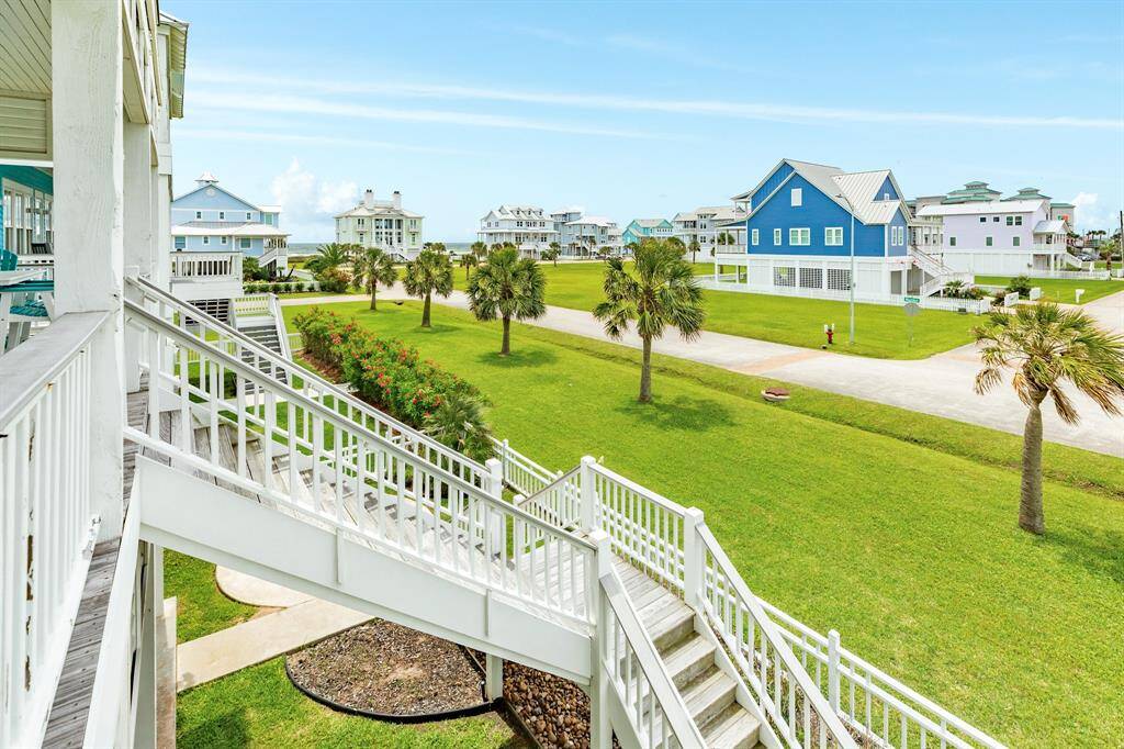 This photo showcases a coastal neighborhood with charming, elevated homes and lush green lawns. The view includes a well-maintained landscape with palm trees, a clear sky, and a vie of the Gulf, creating a serene and picturesque setting.