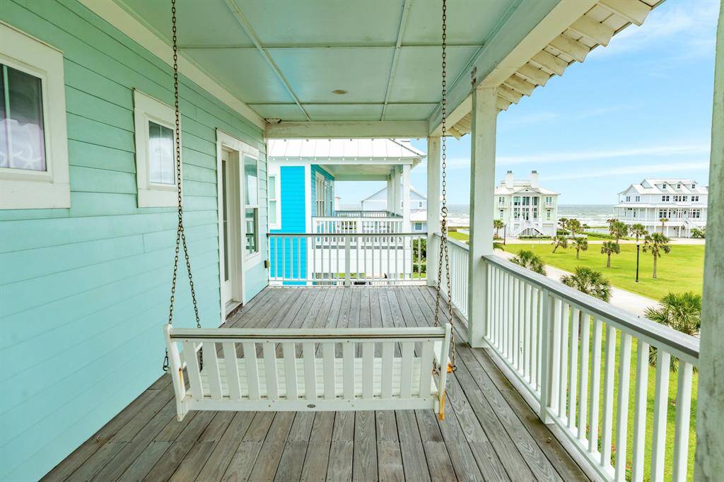 Charming coastal home with a spacious covered deck featuring a swing. The view overlooks a lush lawn and nearby beach houses with Gulf views, perfect for relaxation and enjoying the sea breeze.
