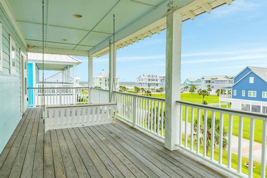 This photo showcases a charming porch with a wooden swing, offering a relaxing view of neighboring homes and a glimpse of the ocean. Ideal for enjoying serene mornings or sunset views in a coastal community.