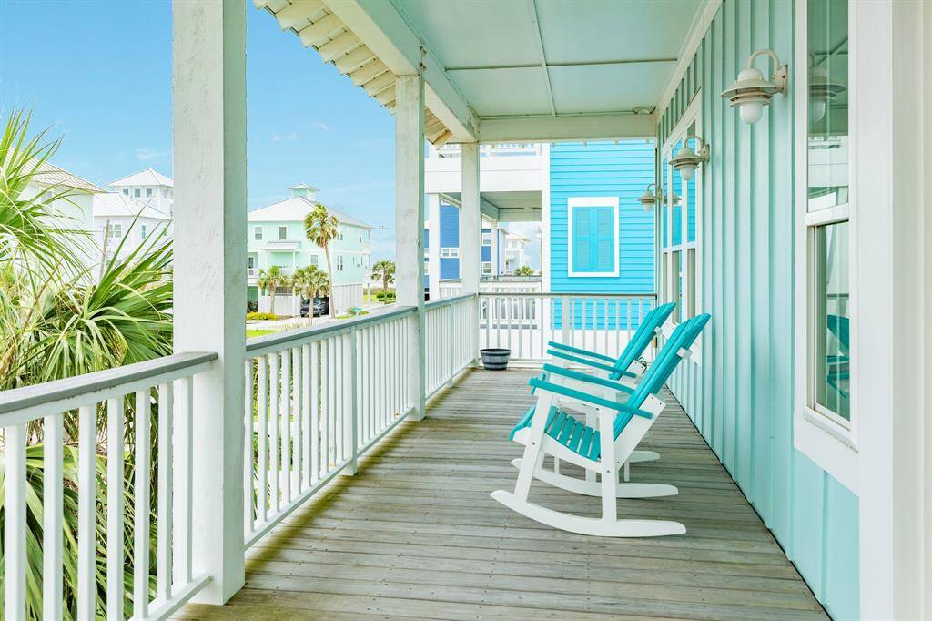 This inviting deck features bright rocking chairs and a charming, coastal vibe. The space is perfect for relaxing while enjoying views of neighboring homes and lush palm trees.