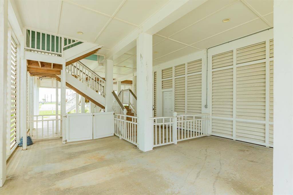 This photo shows a spacious, covered outdoor area with white railings and stairs leading up. It features louvered walls for ventilation and is ideal for parking or storage.