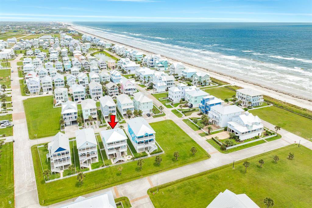 This aerial photo features Beachside Village, a coastal neighborhood with modern homes. The area features neatly arranged  homes with spacious lawns, set along a scenic beach, offering stunning ocean views and a serene environment.