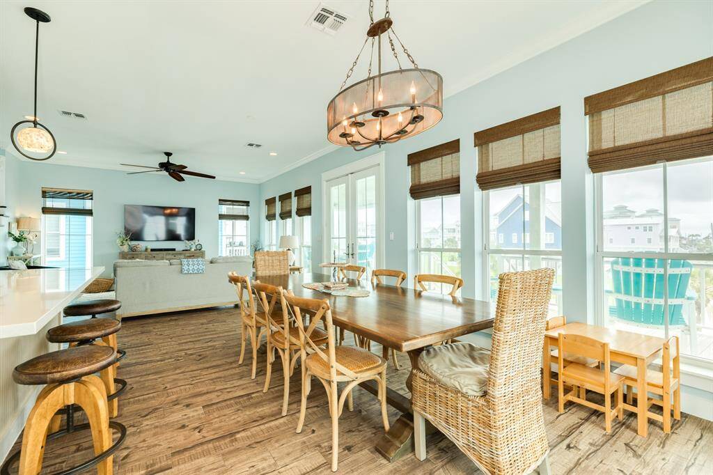 This open-concept living space features a bright, airy design with large windows, hardwood floors, and a modern dining area. The kitchen island offers additional seating with stylish bar stools. Ideal for family gatherings and entertaining.