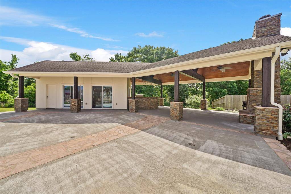 This photo showcases a spacious covered patio area with stone columns and a ceiling fan, connected to the guest house with sliding glass doors. The setting is open and surrounded by greenery, offering a versatile outdoor space. Entertainment capital of the world.