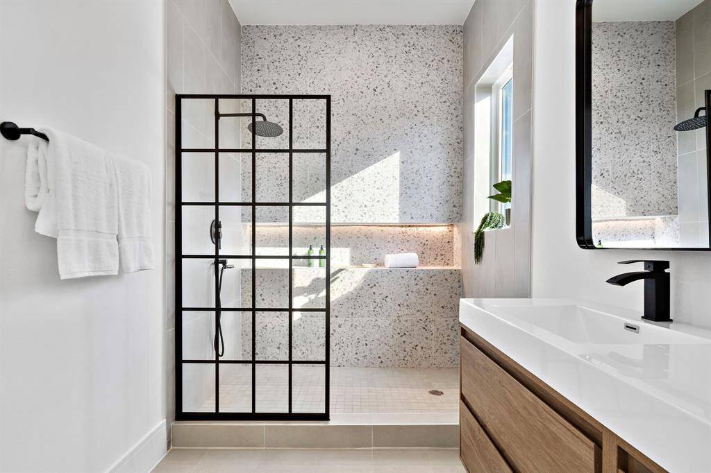 Featuring stunning large mosaic tiles that extend to the ceiling, a sleek paneled glass divider, a luxurious rainfall showerhead, and a convenient shower wand, this shower is a spa-like retreat.