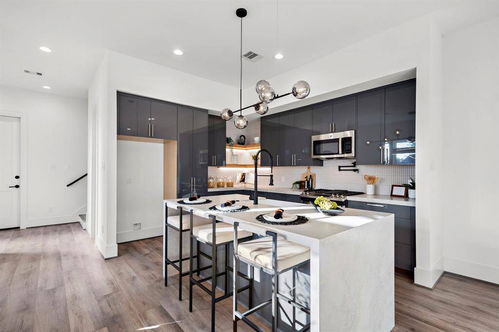 Step into a modern kitchen designed to impress, featuring chic pendant lighting, sleek lacquered-finish cabinets, a convenient lazy Susan, and ample storage space to keep everything organized and within reach.