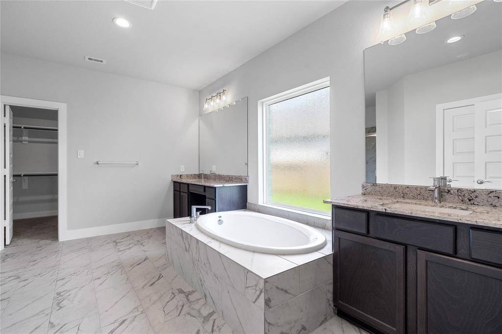This primary bathroom is definitely move-in ready! Featuring a separate garden tub for soaking after a long day with custom tile detailing, rain glass window, stained cabinets with countertops, spacious walk-in closet with shelving, high ceilings, custom paint, mirrors, sleek and dark modern finishes.