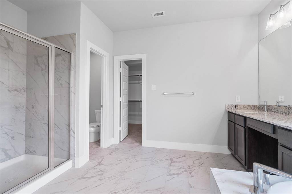 This additional view of the primary bath showcases the large walk-in shower with tile surround, privacy toilet area, and spacious walk-in closet.