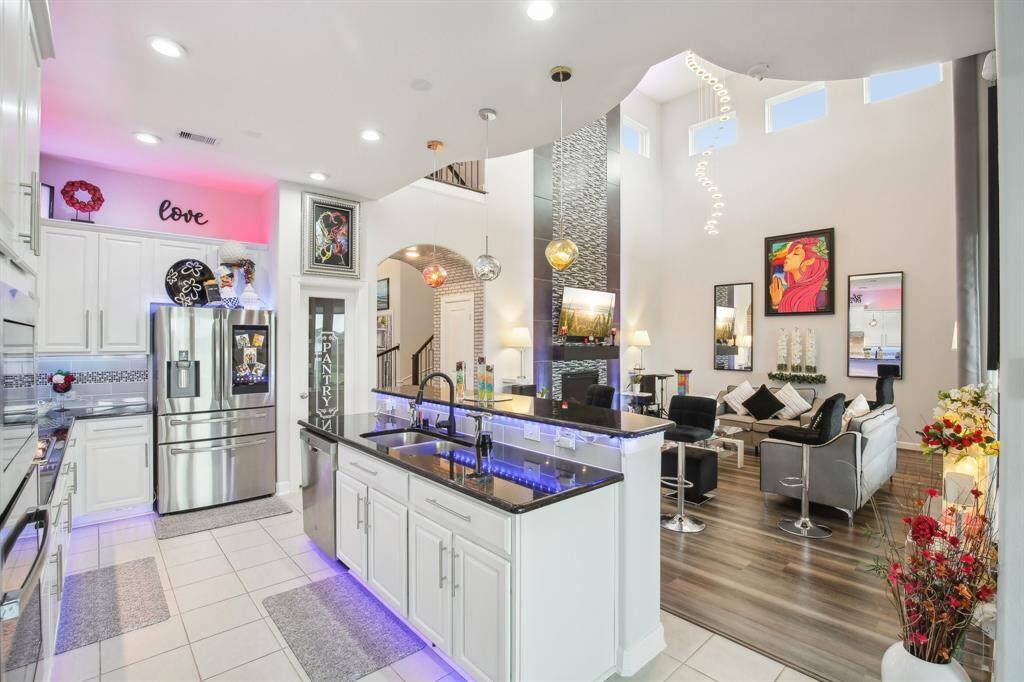 This modern home features an open-concept kitchen and living area with high ceilings and abundant natural light. The kitchen boasts sleek white cabinetry, stainless steel appliances, and stylish lighting