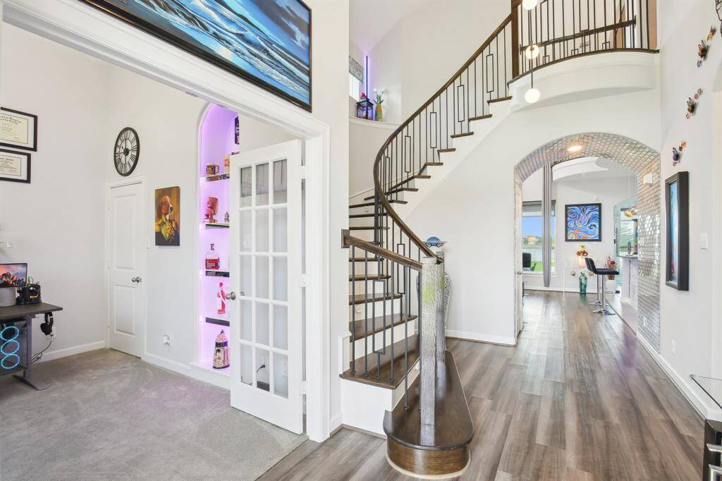 This home features a modern entryway with a striking curved staircase, open layout, and sleek flooring. A cozy office space is visible to the left, and the living area ahead is bright with large windows, offering plenty of natural light.