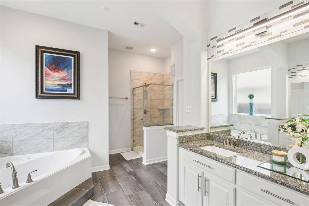 This bathroom features a modern design with a spacious glass-enclosed shower, elegant soaking tub, and dual-sink granite vanity. The room is accented with stylish tile work and bright natural lighting.
