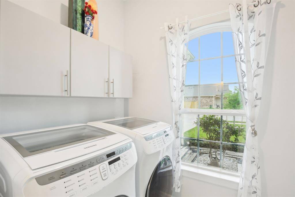 Bright laundry room featuring modern appliances, ample overhead storage, and a window with a view of the garden, creating a pleasant and functional space.
