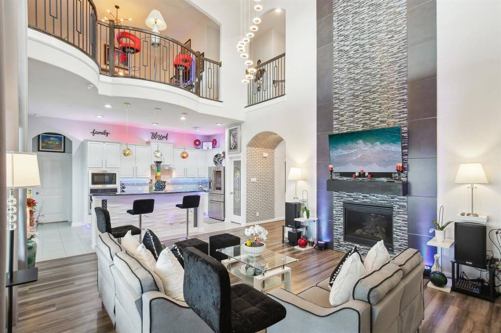 This spacious living area features a modern, open-concept design with high ceilings, a sleek stone fireplace, and a stylish railing overlooking the room. The bright kitchen includes a large island with bar seating, and contemporary appliances. Ideal for entertaining and family gatherings.