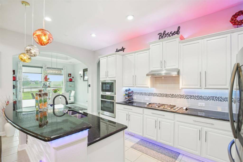 This modern home features an open-concept kitchen and living area with high ceilings and abundant natural light. The kitchen boasts sleek white cabinetry, stainless steel appliances, and stylish lighting