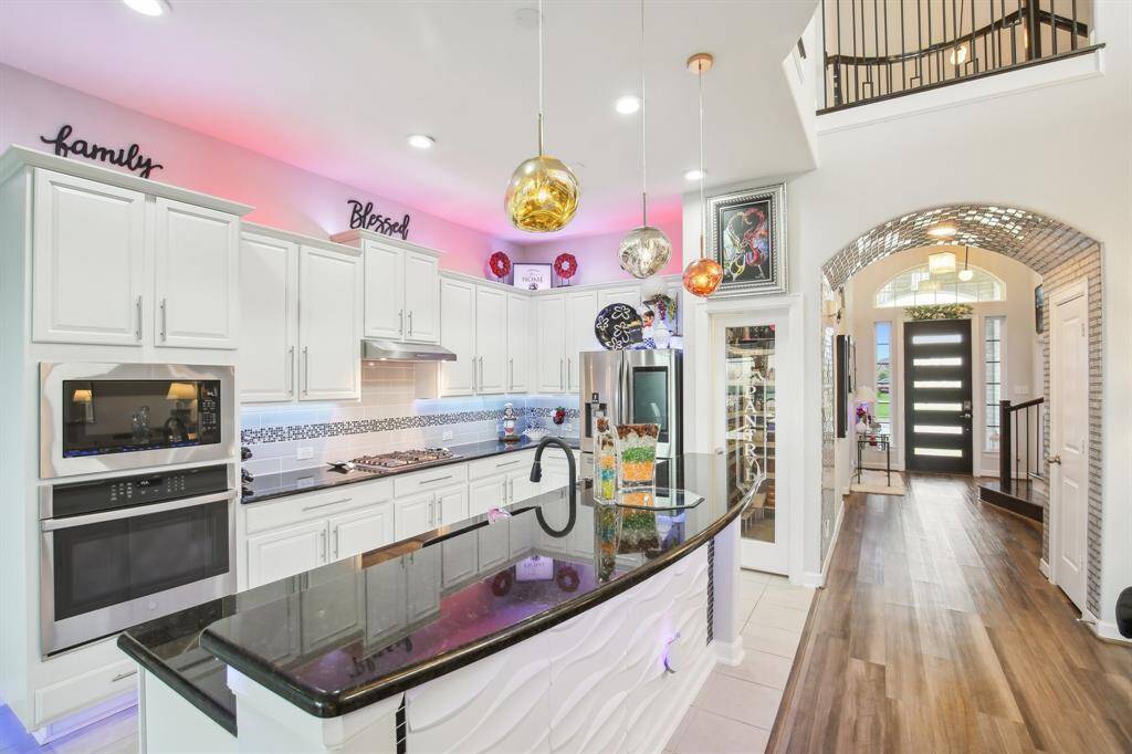 This modern home features an open-concept kitchen and living area with high ceilings and abundant natural light. The kitchen boasts sleek white cabinetry, stainless steel appliances, and stylish lighting