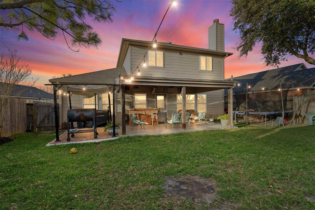 Charming two-story home with a spacious backyard featuring a covered patio, string lights, and a barbecue area. Ideal for outdoor entertaining and relaxation.
