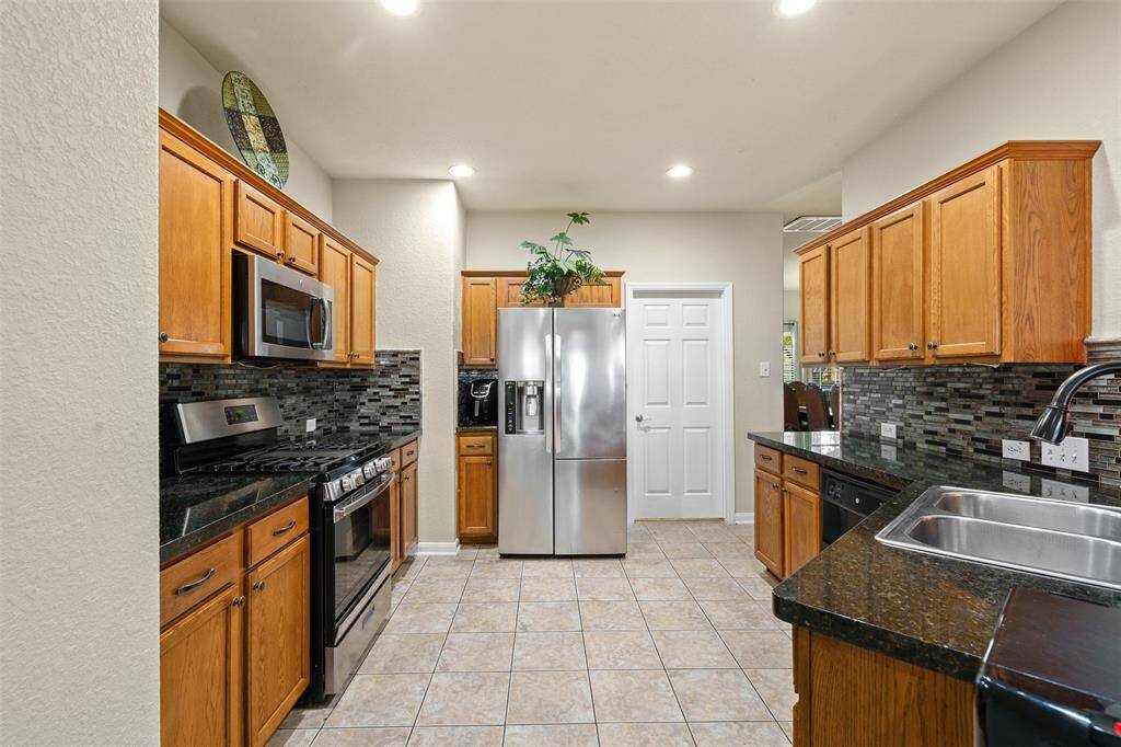 This kitchen features modern stainless steel appliances, granite countertops, and warm wood cabinetry. It has a sleek tile backsplash, ample storage, and a tiled floor for easy maintenance.