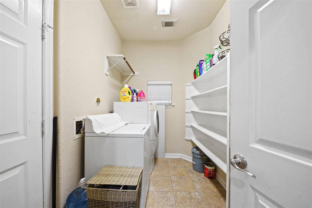 This photo shows a well-organized laundry room with a washer and dryer, ample shelving for storage, and a small window for natural light. The space is clean and features tiled flooring.