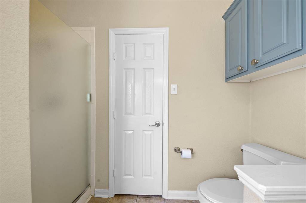 This bathroom features a tiled shower with a frosted glass door, a white door, a toilet, and blue wall-mounted cabinets, offering practical storage and a clean design.