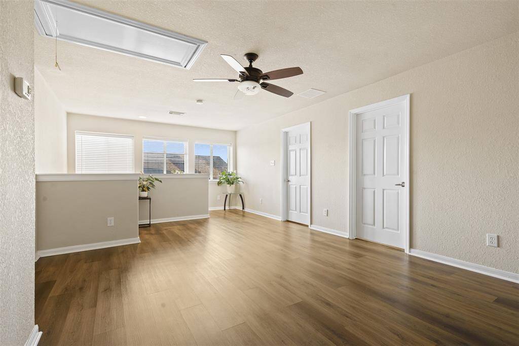 Bright and spacious room with light wood flooring, neutral walls, and a ceiling fan. Features multiple doors and large windows, offering plenty of natural light. Ideal for a living area or home office.