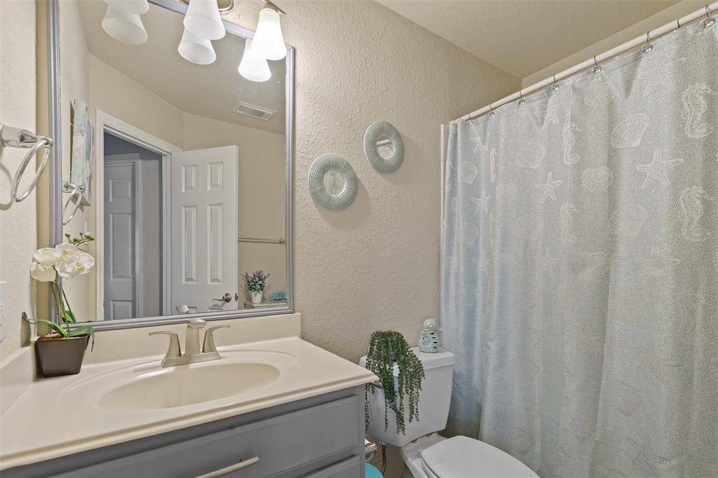 This bathroom features a clean design with a large mirror, modern lighting, and a light-colored vanity. It includes a shower with a decorative curtain and tasteful decor, creating a welcoming and functional space.