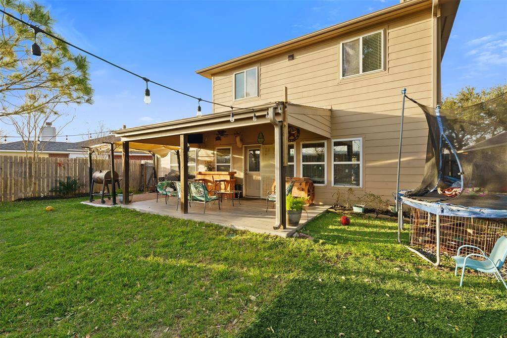 Charming two-story home with a spacious backyard, featuring a covered patio perfect for outdoor gatherings. The yard includes a trampoline and is bordered by a wooden fence, offering privacy and ample space for activities.