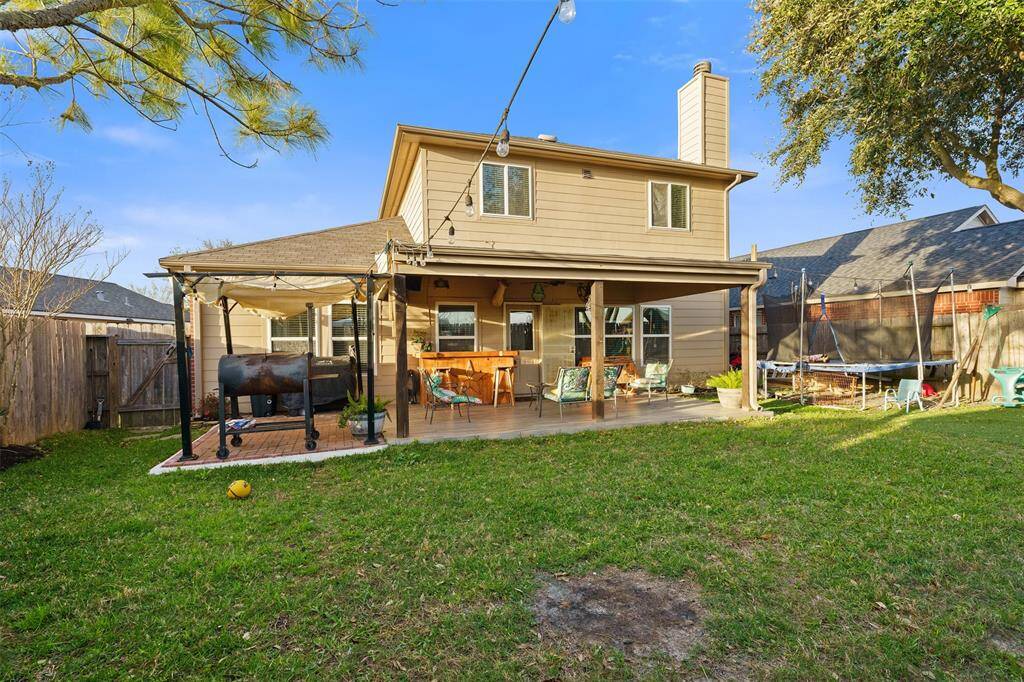 This inviting backyard features a spacious patio with a pergola, ideal for outdoor entertaining. The well-maintained lawn is perfect for family activities, and there's a barbecue grill for cooking. A trampoline adds a fun element for kids, all within a fenced, private setting.