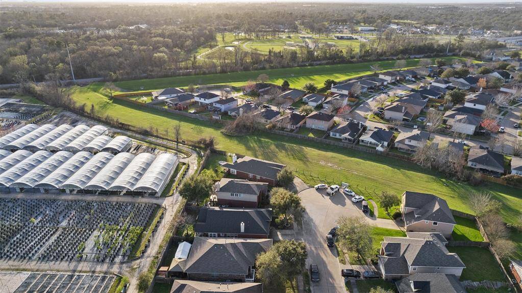 This aerial photo shows a suburban neighborhood with well-maintained homes next to a large green space and a nursery. It offers a peaceful environment with ample greenery and a sense of community.