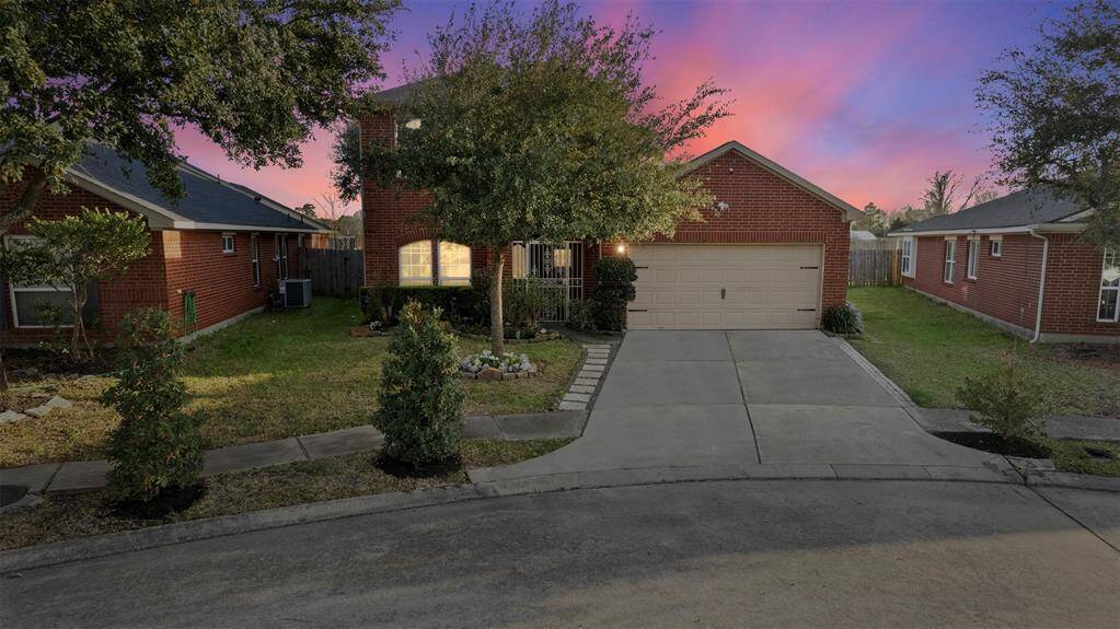 Charming red brick home with a two-car garage, nestled on a quiet street. The front yard features mature trees and well-kept landscaping, all under a beautiful sunset sky.