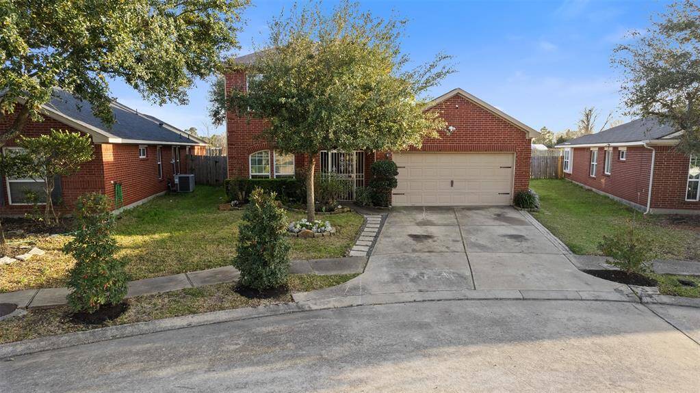 Charming red brick home featuring a two-car garage and a neat driveway. The front yard is landscaped with small trees and shrubs, offering a welcoming entrance.