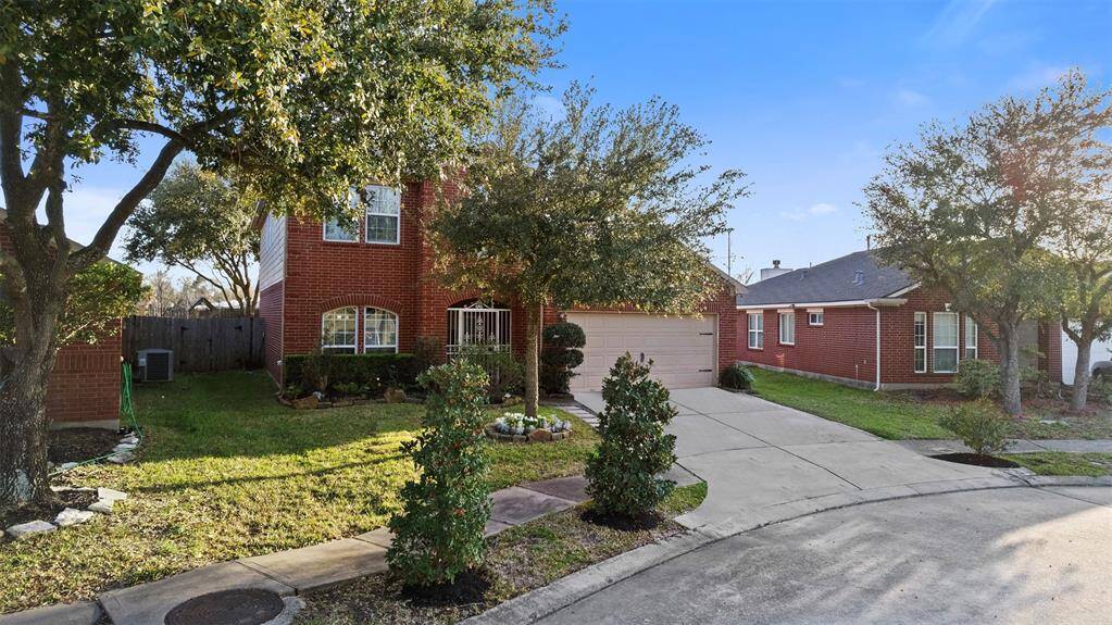 This photo shows a charming, two-story red brick home with a front lawn and mature trees. It features a two-car garage and a curved driveway, offering a welcoming and spacious exterior.