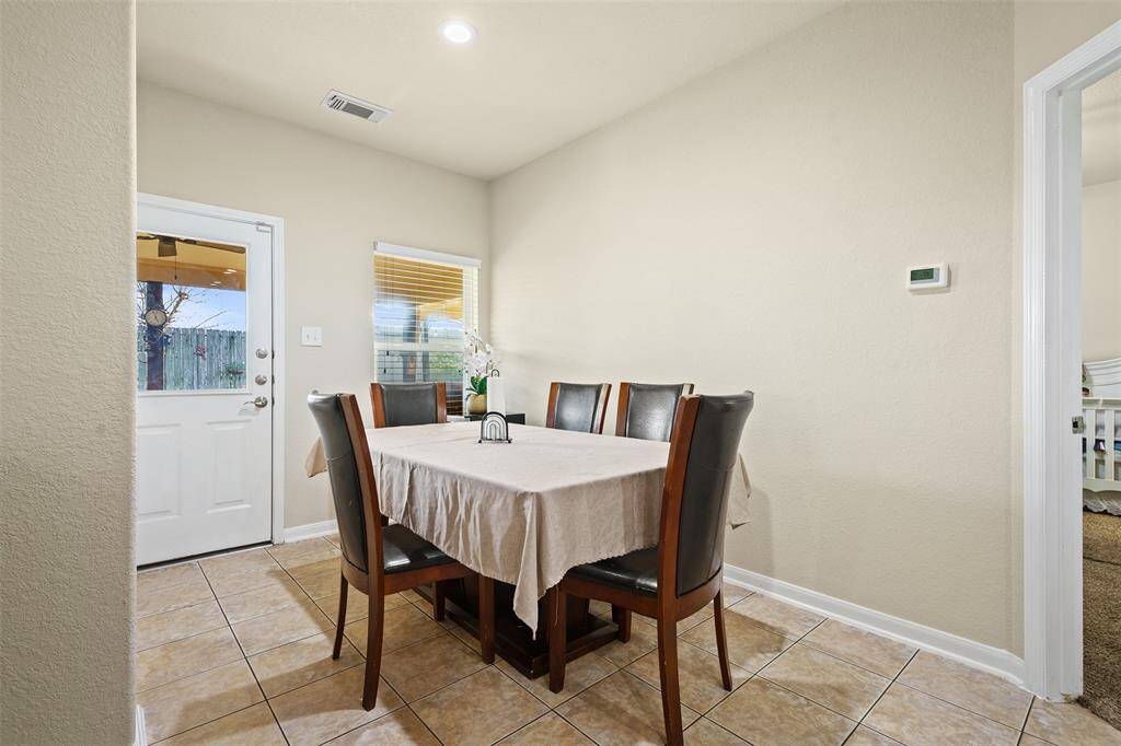 This photo shows a cozy dining area with a six-seat table, tile flooring, and neutral walls. There's a door leading outside and a window providing natural light, creating a welcoming atmosphere.