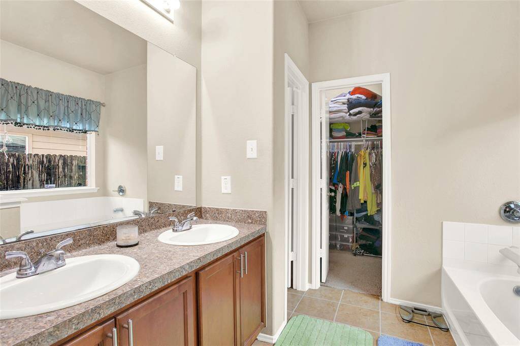 Discover the elegance of this pristine bathroom, boasting a sleek dual-sink vanity set atop a stunning granite countertop, complemented by abundant cabinetry and an expansive mirror. An adjoining walk-in closet features thoughtful built-in storage, optimizing organization and convenience.