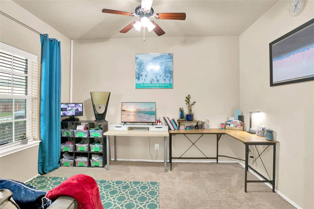 Discover a bright and inviting home office featuring a breezy ceiling fan, expansive desk space, and easy access —all bathed in natural light.