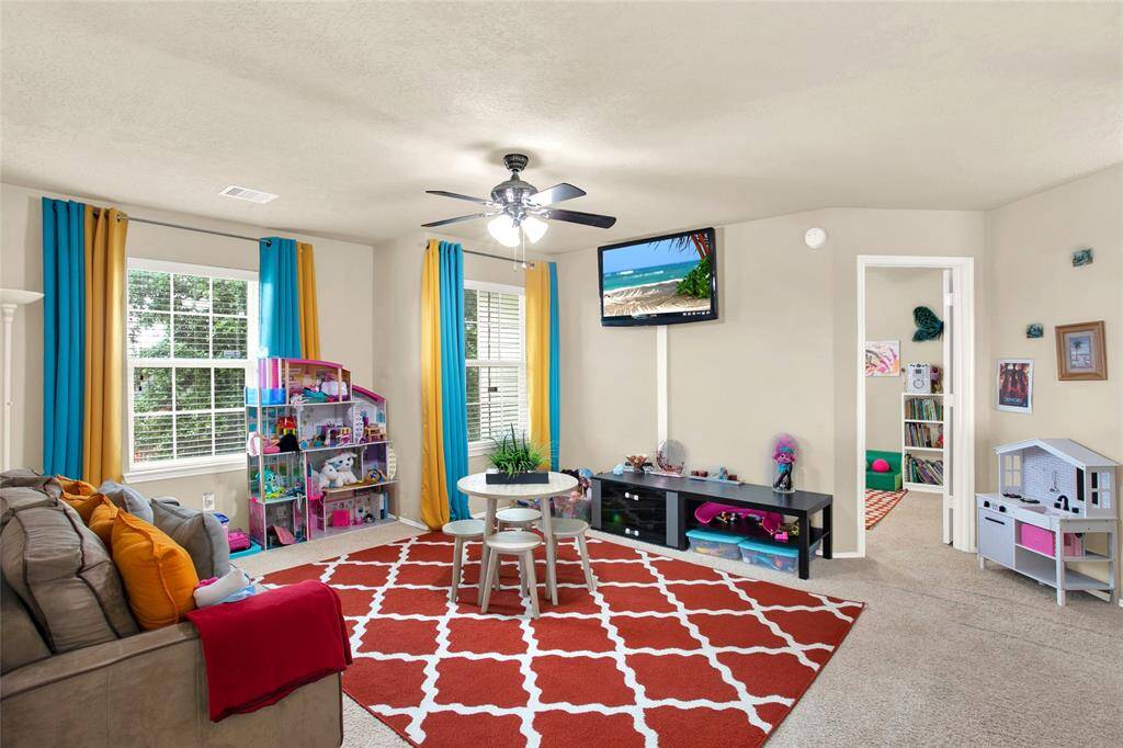 Discover a sunlit haven ideal for family living, showcasing expansive windows that bathe the room in natural light, enhanced by a comforting ceiling fan, and a charming seating nook perfect for relaxation and play.
