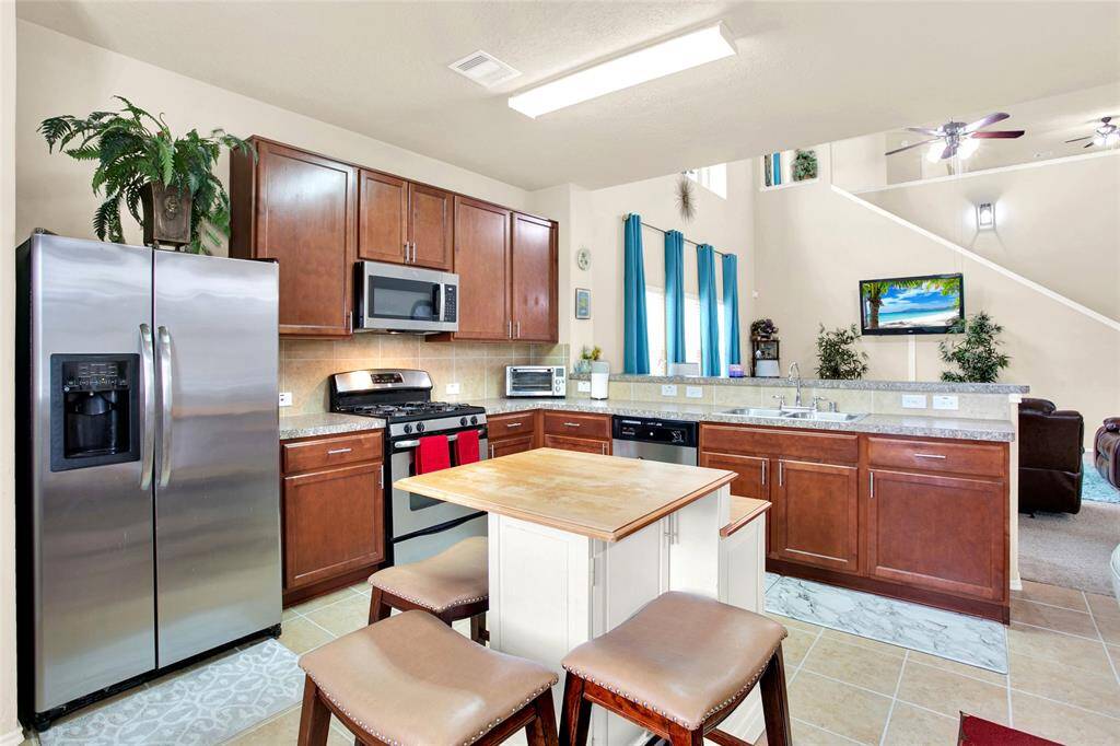 Experience the fusion of ease and convenience in this sleek kitchen, boasting stainless steel appliances, rich wooden cabinets, and elegant granite counters. The open-plan design seamlessly connects to a sunlit living space with soaring ceilings for an expansive feel.