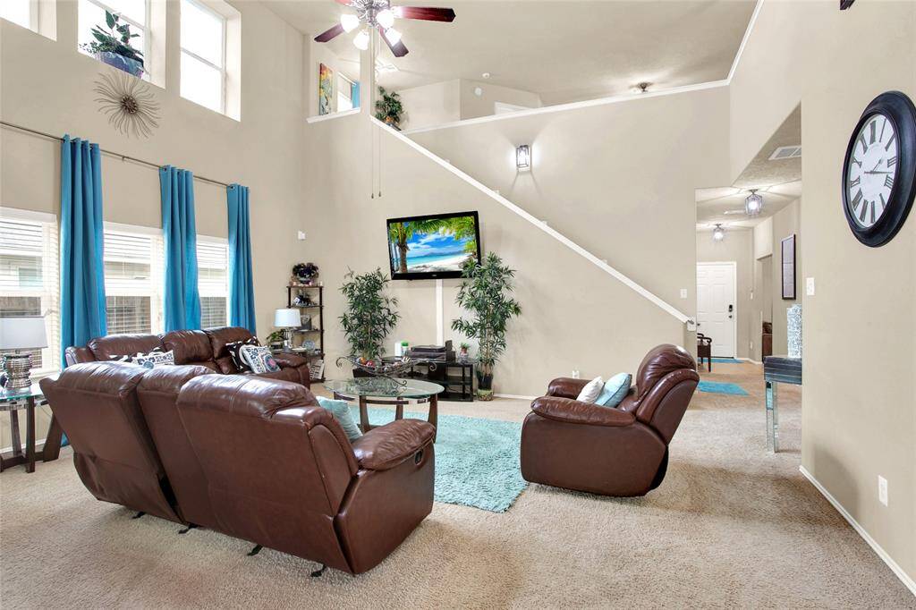 Discover the airy elegance of this living room, boasting soaring ceilings, expansive windows for abundant natural light, and a graceful staircase ascending to the upper floor. Plush carpeting underfoot enhances the room's inviting ambiance.