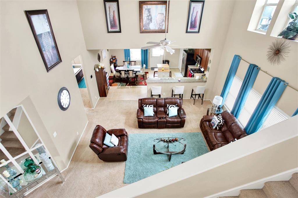 Discover an airy, sunlit haven in this open-plan living space boasting soaring ceilings and expansive windows. Elegant mixed flooring unites cozy comfort with chic design, complemented by a sleek ceiling fan to ensure year-round relaxation.