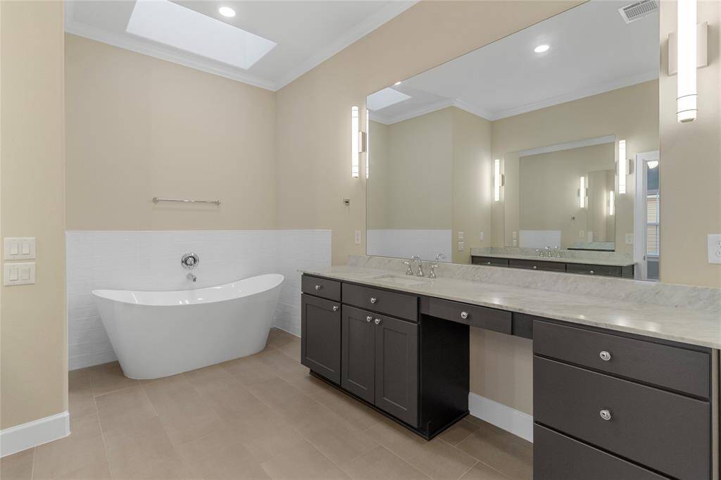 This bathroom features a modern freestanding tub, dual sinks with a large mirror, elegant lighting, and a skylight, creating a bright and contemporary space.