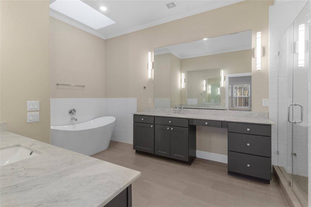This bathroom features a modern freestanding tub, dual sinks with a large mirror, elegant lighting, and a skylight, creating a bright and contemporary space.