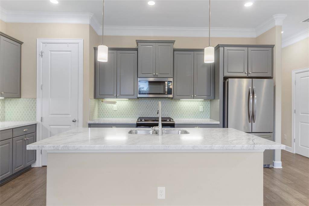 Modern kitchen features sleek gray cabinetry, stainless steel appliances, and a spacious island with a marble countertop. Pendant lighting and a subtle backsplash add a stylish touch, while the open layout provides ample space for cooking and entertaining.