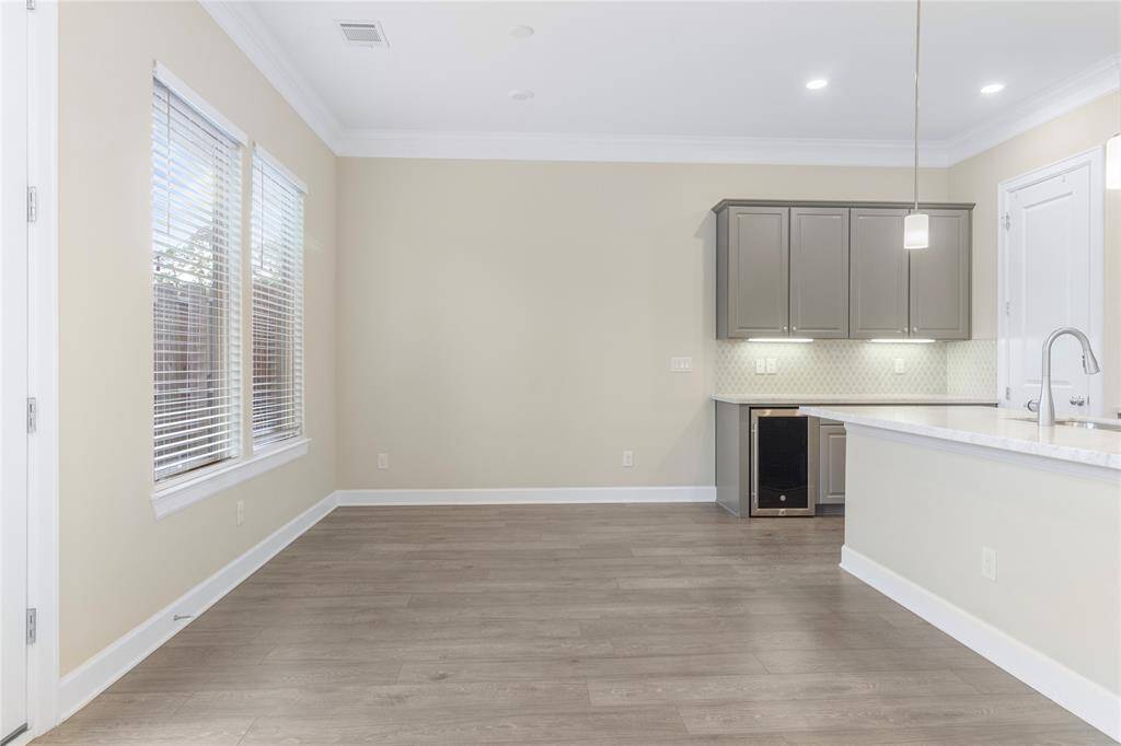 Bright, open-concept kitchen and dining area with light wood floors, neutral walls, and ample natural light from large windows. Features include modern cabinetry, a breakfast bar, and under-cabinet lighting.