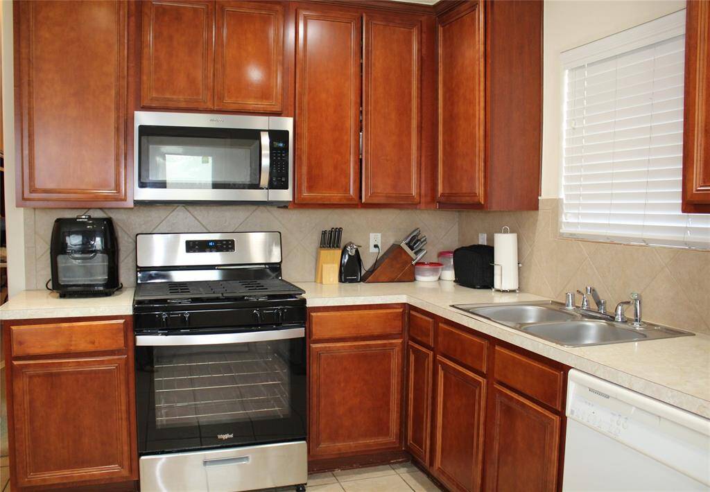 Kitchen has stainless microwave and gas range. Neutral color counter tops, black splash, and floor tile.