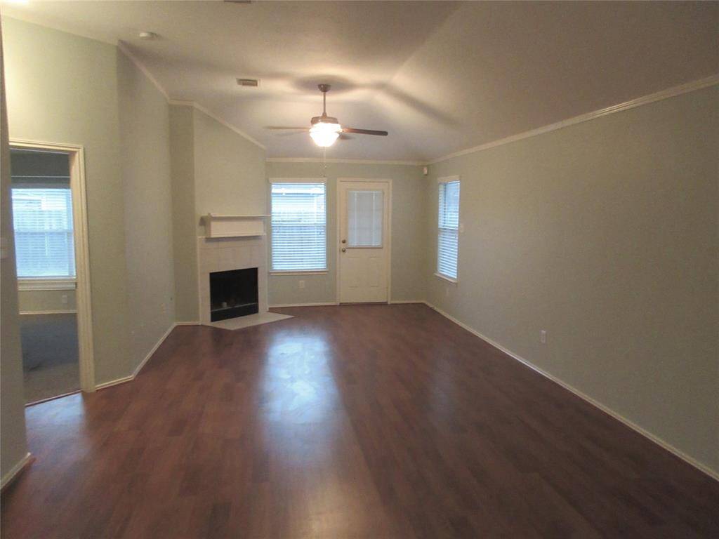 This spacious living room features a cozy corner fireplace, and abundant natural light from multiple windows. The ceiling fan provides comfort, and there's easy access to the outdoors through a door at the back.